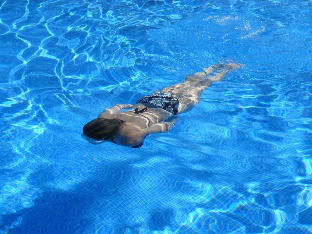 A woman gracefully swimming underwater in a sunlit pool, showcasing freestyle swimming.